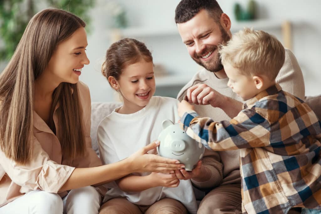 happy family--husband, wife, and two children, happy, laughing putting money into a piggy bank.